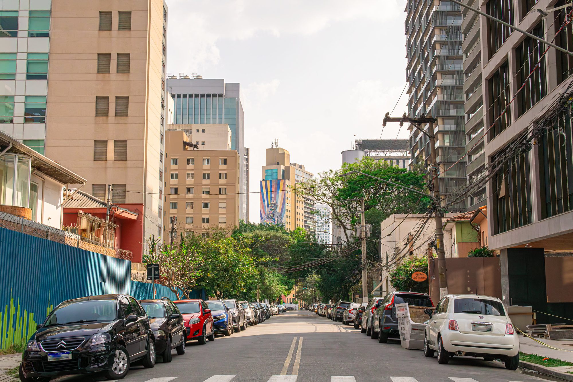 Rua de Pinheiros ao fim da tarde, com carros estacionados e prédios ao fundo
